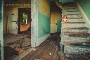 Doll sitting on the edge of a falling apart staircase inside an abandoned house.