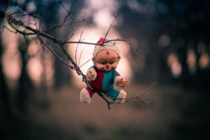 Creepy clown-dressed doll propped up in the branches of a tree with no leaves.