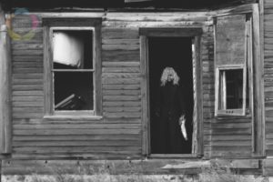Ghostly figure with a dolls head in teh door frame of an abandoned house