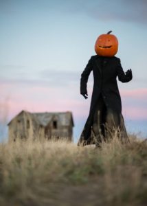 A pumpkin-head, black robed figure with an abandoned house in the background.