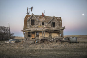 Creepy photograph of a falling apart abandoned home in an open field.