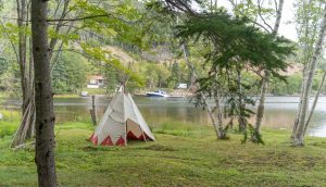 Tipi set up along a river surrounded by trees