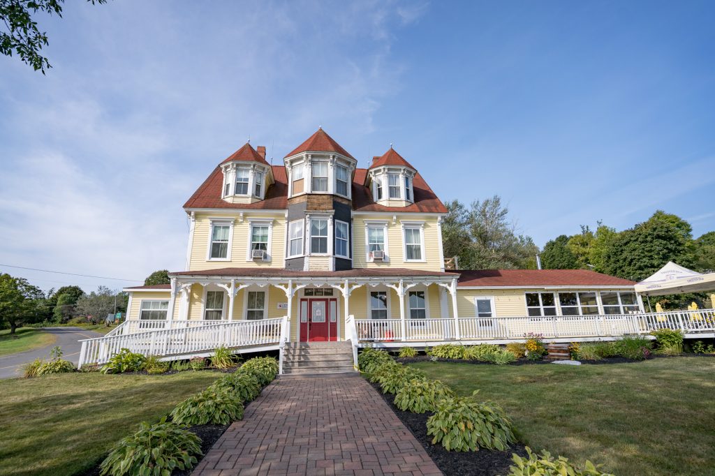 Big yellow mansion with three peaked turret rooms and a white verandah and wainscotting across the front.