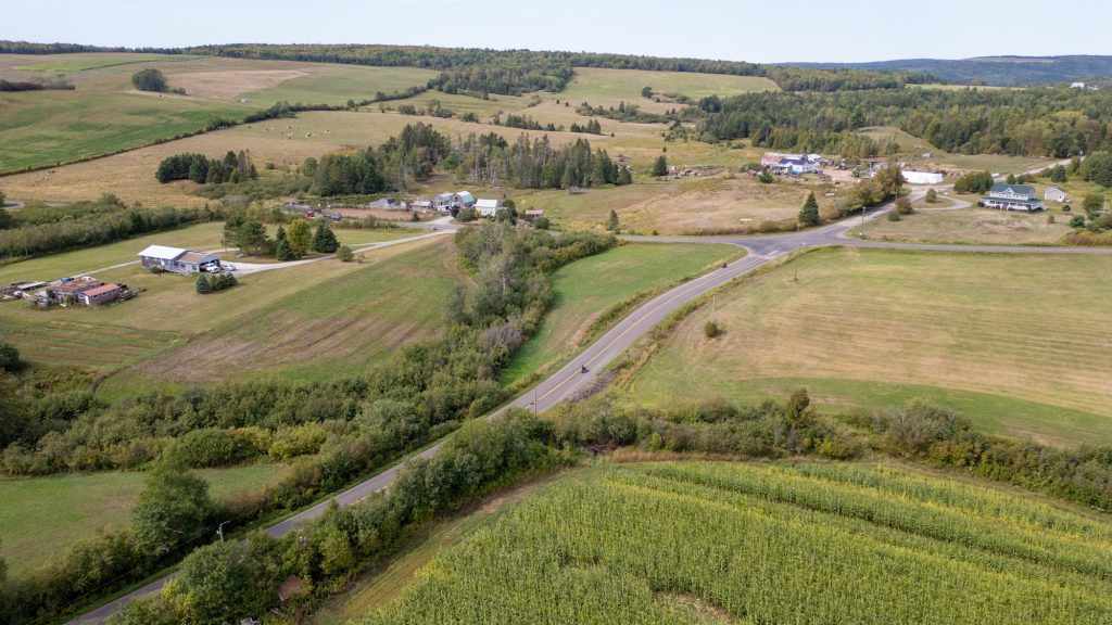 A highway running through gently rolling farmland with scattered farmhouses and yards.