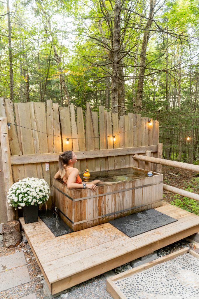 A woman in a wooden outdoor tub doing a cold plung.