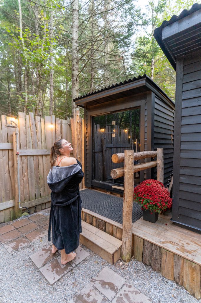 A woman in a robe walking up to a sauna building outdoors. 