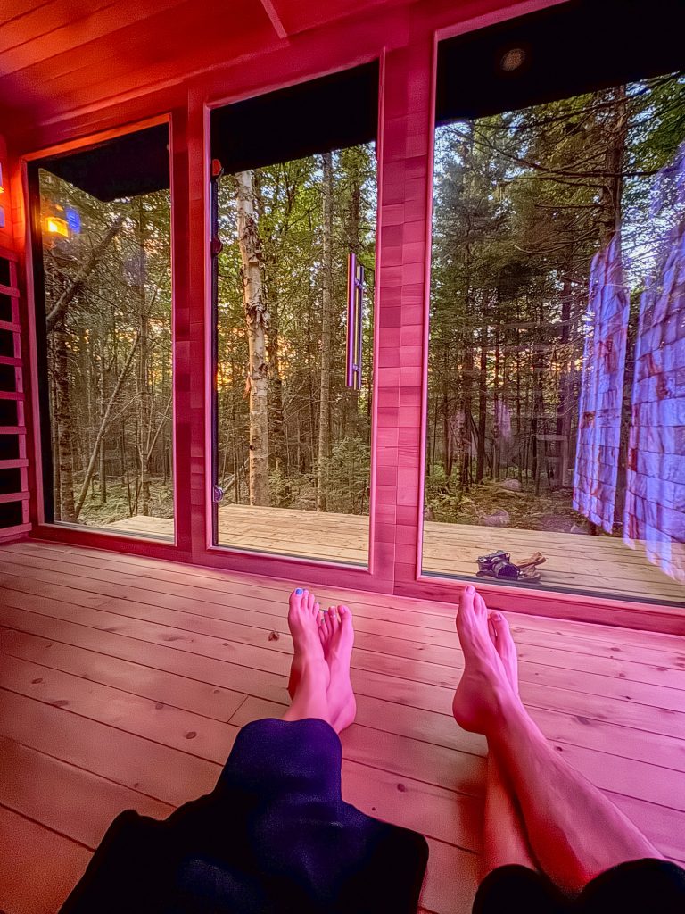Legs and feet of two people inside a wooden building with windows overlooking a forest. 