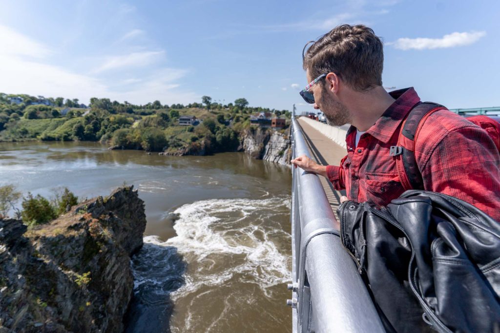 A man in a red plaid shirt overlooking the railing on a bridge to the Reversing Falls in Saint John, New Brunswick.