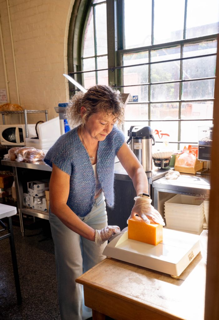 A woman cutting a slice of cheese on a scale.