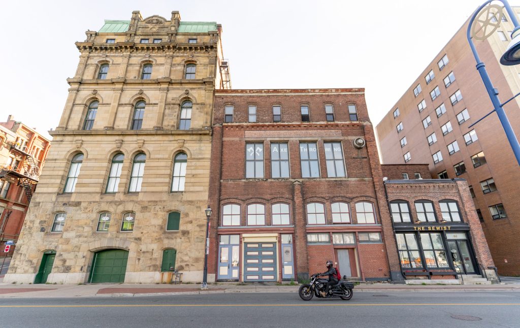 A motorcycle riding in front of brown and red bricked buildings in Saint John, New Brunswick.