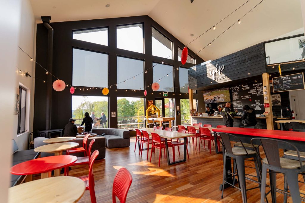 Interior of Yip Cider with red chairs and tables, a bar to order at and big peaked windows.